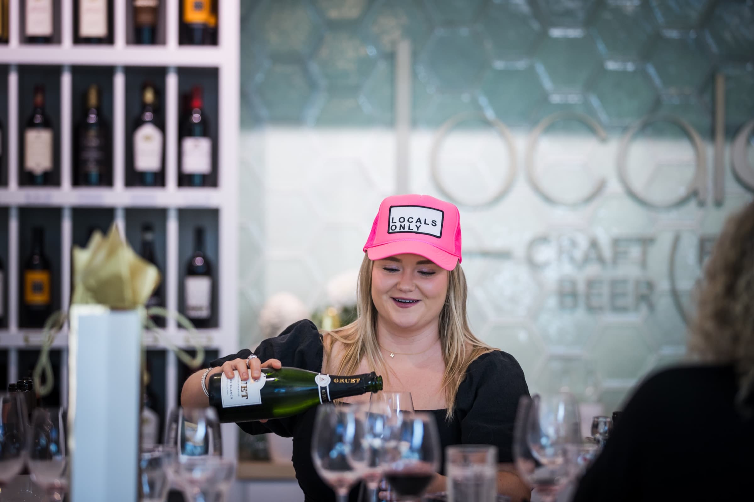 A Locals team member in a Locals Only cap pouring sparkling wine for guests