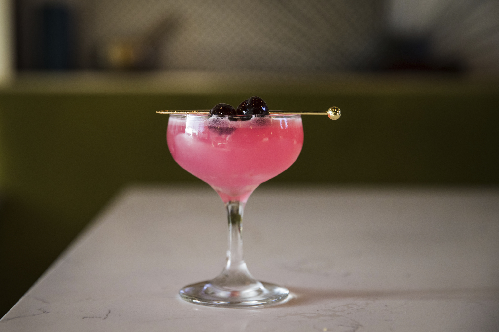 Pink cocktail in a coupe glass garnished with two cherries