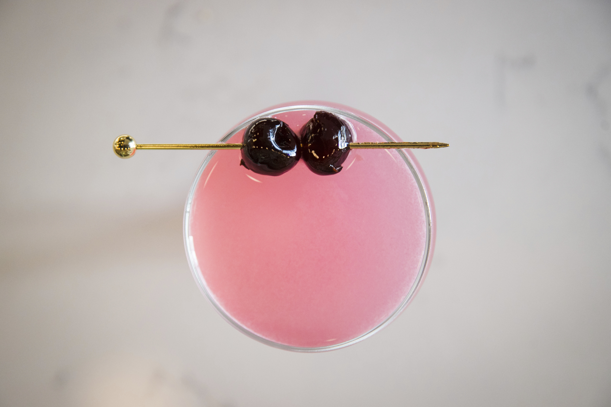 Overhead view of a pink cocktail garnished with two cherries
