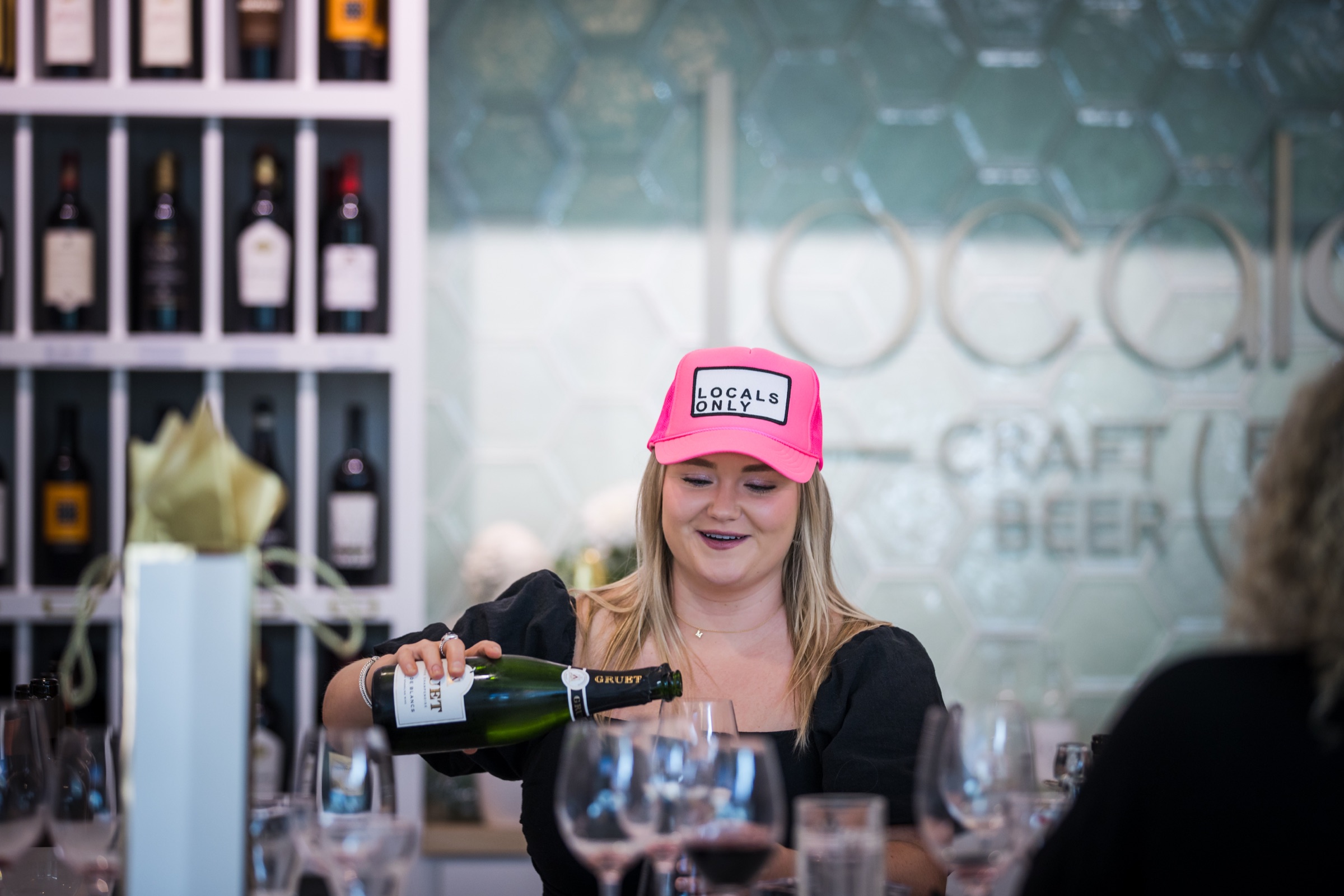 A Locals team member in a Locals Only cap pouring sparkling wine for guests
